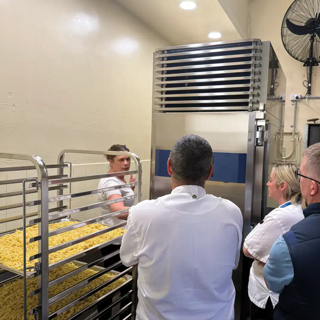 Staff in white coats observe a large stainless steel rack filled with golden French fries in a food processing area.