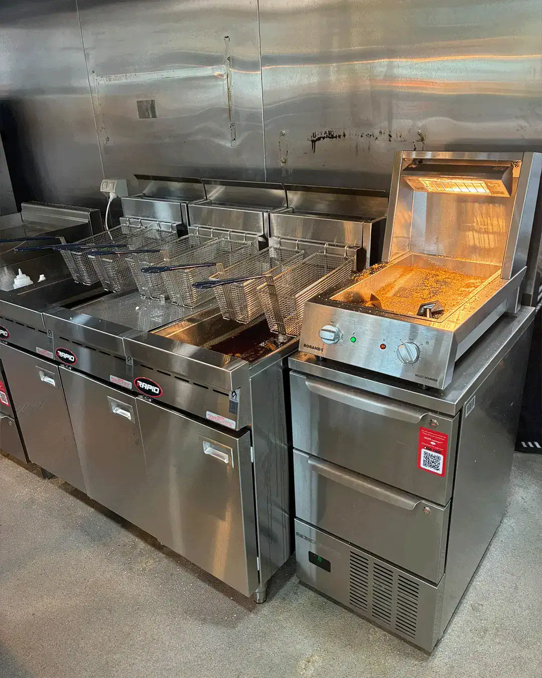Commercial stainless-steel deep fryer station with multiple baskets and a countertop fryer on the right.